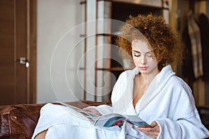 Cute lovely serene female sitting at home and reading magazine