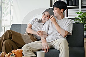 A cute and lovely young Asian couple is hugging while enjoying watching TV on a couch