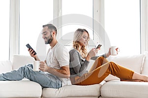 Cute loving couple indoors at home using mobile phones
