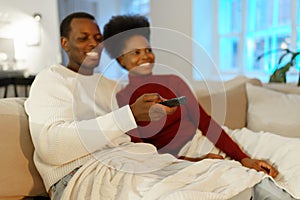 Happy african couple chilling at home. Man change channels on tv with remote control and hug woman