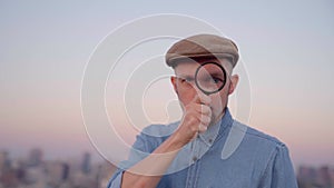 Cute male making big eye with magnifying glass with urban view