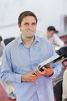 Cute male teacher holding some files while posing in his classroom