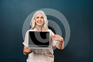 Cute mature old woman showing display of laptop computer pointing.