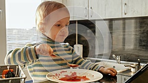 Cute messy boy eating soup with spoon and watching cartoons. Domestic food, gadget addiction, children healthy nutrition