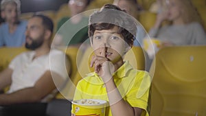 Cute Middle Eastern boy showing hush gesture in cinema. Portrait of happy little kid enjoying film in movie theatre