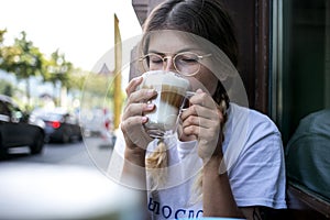 Cute pretty young woman drinks coffee milk foam