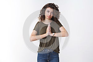 Cute miserable-looking young caucasian curly-haired woman sulking making pitty sad grimace press palms together pray photo