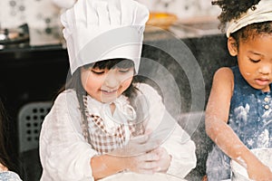 Cute mixed race and African American kid girls baking or cooking together in home kitchen