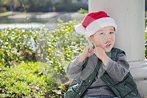 Cute Mixed Race Boy in Santa Hat eating Candy Cane