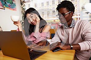 Cute mixed race couple of teenagers enjoying milkshake at cafeteria, first date