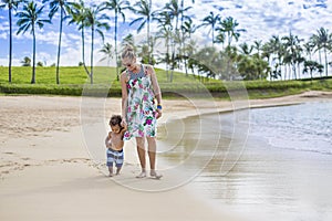 Cute mixed race little boy walking along the beach with his mother on a tropical island vacation.
