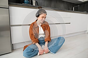 Cute modern girl on kitchen floor at home, listening music in wireless headphones, having fun