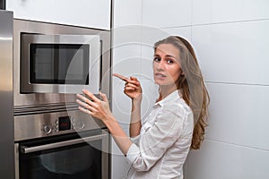 Cute modern woman in the kitchen opening the microwave and disappointed in the result of cooking.