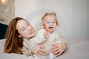 Cute mom and baby daughter lie down, play and hug in bed. games with children.