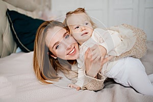 Cute mom and baby daughter lie down, play and hug in bed. games with children.
