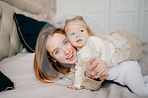 Cute mom and baby daughter lie down, play and hug in bed. games with children.