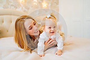 Cute mom and baby daughter lie down, play and hug in bed. games with children.