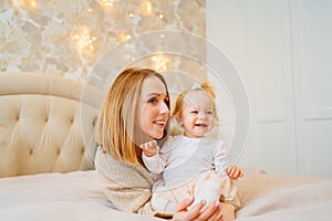 Cute mom and baby daughter lie down, play and hug in bed. games with children.