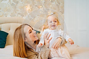 Cute mom and baby daughter lie down, play and hug in bed. games with children.