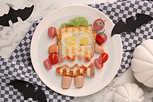 Cute monster sandwich with cherry tomatoes, fried eggs and sausages on white marble table, flat lay. Halloween snack