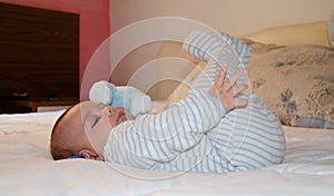 Cute 4 months old baby boy lying on bed and playing with his legs