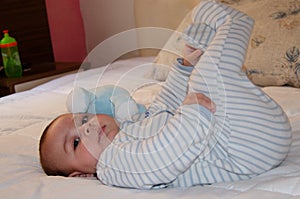 Cute 4 months old baby boy lying on bed and playing with his legs