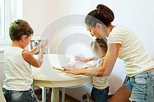 A cute mother and her children sculpt dough in the kitchen