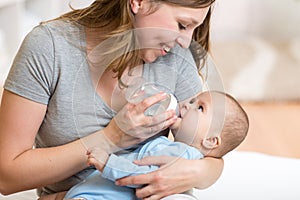 Cute mother at home feeding baby with a milk bottle