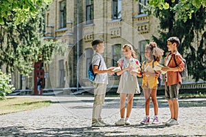 Cute multicultural schoolkids talking while standing in schoolyard and holding books