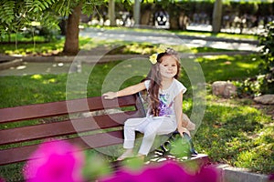 Cute musical baby child girl with brunette hairs and stylish wear enjoying life sitting on wooden chair bench in summer awesome pa