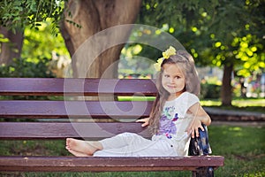 Cute musical baby child girl with brunette hairs and stylish wear enjoying life sitting on wooden chair bench in summer awesome pa photo