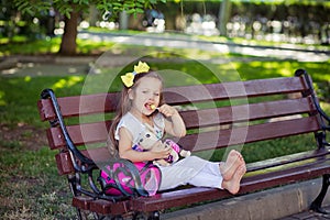 Cute musical baby child girl with brunette hairs and stylish wear enjoying life sitting on wooden chair bench in summer awesome pa photo