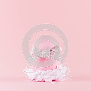 Cute naivety easter background with pink egg with grey bow in white nest on pastel pink backdrop, square. photo