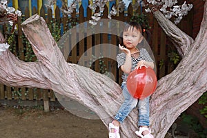 Cute naughty lovely adorable little girl play with balloon and sit by a tree have fun outdoor in summer park happy smile