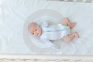 Cute newborn baby boy lying on the back of the crib on the cotton bed at home before going to bed, baby week, the concept of birth