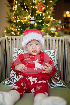 Cute newborn baby boy next to a Christmas tree with festive decoration and ferry lights for New Year celebration