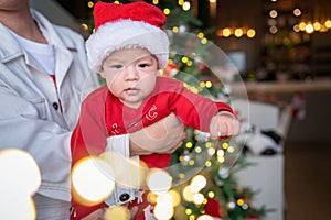 Cute newborn baby boy next to a Christmas tree with festive decoration and ferry lights for New Year celebration