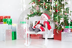 Cute newborn baby boy in Santa costume under Christmas tree