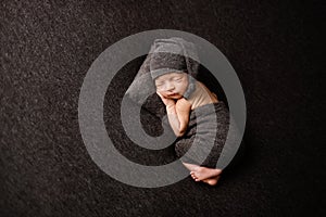 Cute newborn baby on a brown blanket. Sleeping baby on a dark background. Closeup portrait of newborn baby. Baby goods packing tem