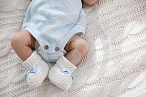 Cute newborn baby in crocheted booties on white knitted plaid, top view. Space for text