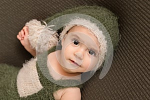 Cute newborn baby in the dark green hat. Happy baby on a green background. Closeup portrait of newborn baby. Baby goods packing te