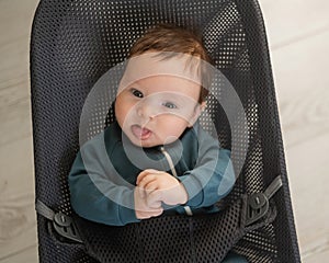 Cute newborn baby dressed in blue overalls sitting in a baby lounger.