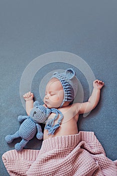 Cute newborn baby girl sleeping with teddy bear on gray blanket.
