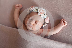 Cute newborn baby girl wearing flower headband peacefully sleeps in funny position.