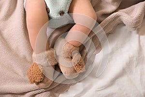 Cute newborn baby in knitted booties lying on bed, top view