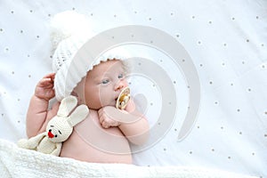 Cute newborn baby in knitted hat with toy lying on bed, top view. Space for text