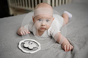 Cute newborn baby lies on bed on his stomach in bodysuit, next to rattle, prevents colic, with crib in background.Baby photo