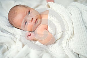 Cute newborn baby lying on bed, covered by a white blanket.