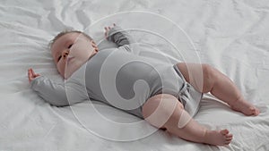 Cute Newborn Baby Lying On Bed At Home, Moving Legs And Arms