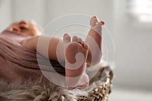 Cute newborn baby lying in wicker basket, focus on legs